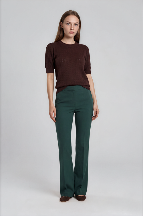 Woman wearing a brown sweater and green pants on a white background