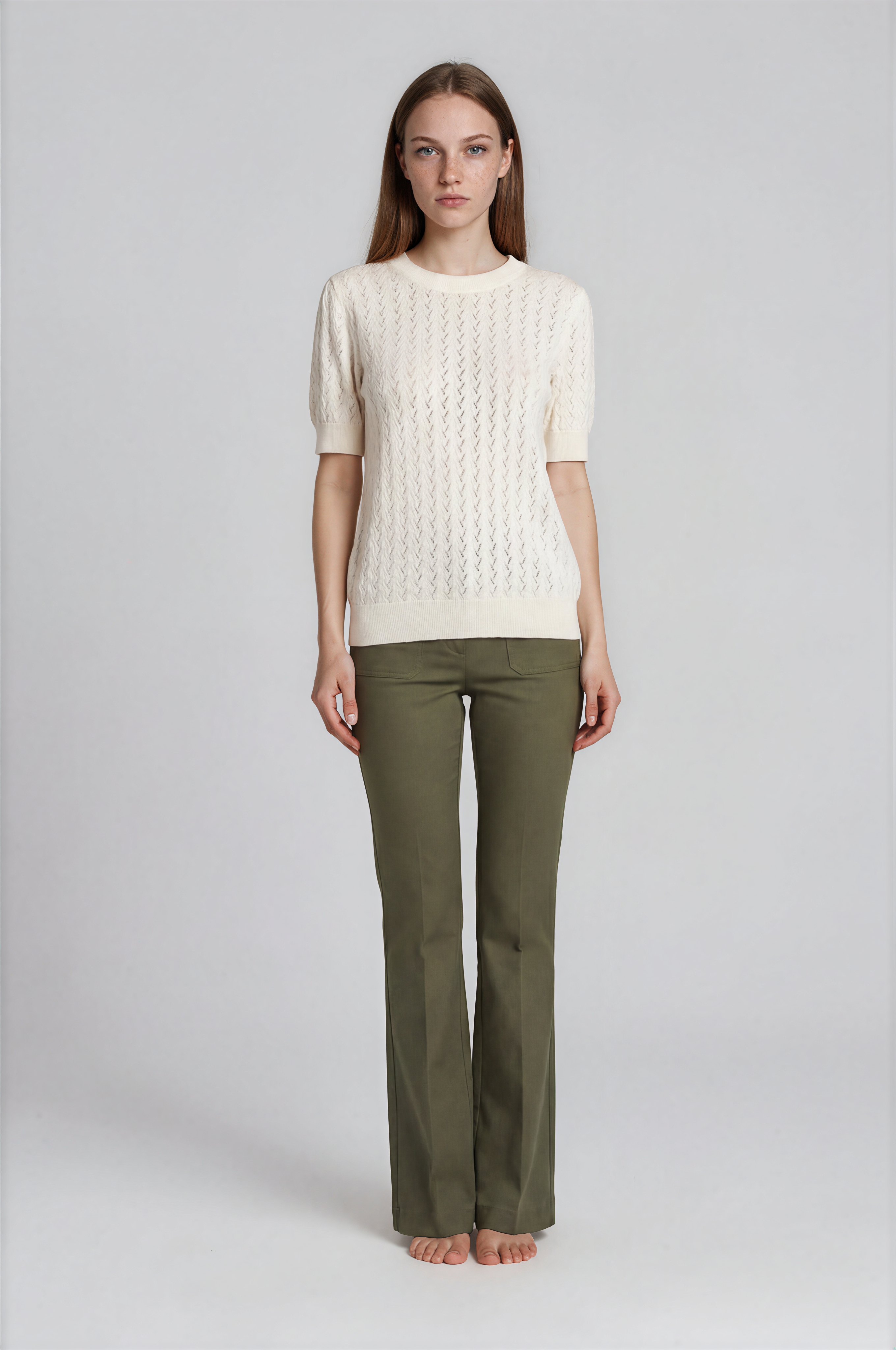 Woman wearing a cream sweater and green pants on a white background