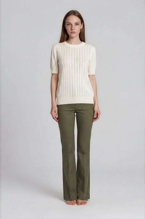 Woman wearing a cream sweater and green pants on a white background